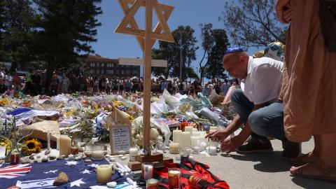 A mourner lights candles as people gather around floral tributes outside Bondi Pavilion in Sydney on December 17, 2025. (Getty Images) Share to Twitter