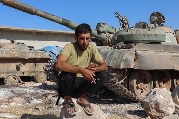 A Syrian rebel fighter checks his phone next to a tank in a rebel training camp near the Bab al-Hawa crossing between Iblib province and Turkey. (Getty Images)