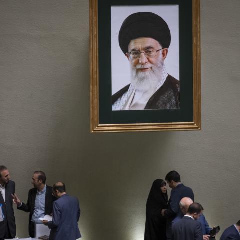 Iranian lawmakers talk to each other, while standing under a framed portrait of Iran's Supreme Leader, Ayatollah Ali Khamenei, during a public session of the Iranian Parliament in Tehran, Iran on April 22, 2025.(Morteza Nikoubazl via Getty Images)