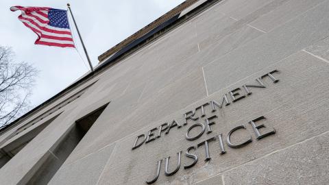 The US flag flies above a sign marking the US Department of Justice headquarters on January 20, 2024, in Washington, DC. (Photo by J. David Ake/Getty Images)