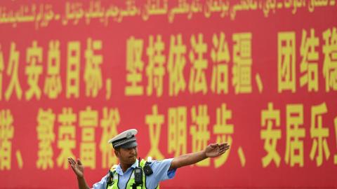 A police officer gestures in front of a propaganda billboard urging "the maintenance of rule of law in Xinjiang" in both Chinese and Uyghur languages in China's northwestern Xinjiang region on July 19, 2023. (Pedro Pardo/AFP via Getty Images)