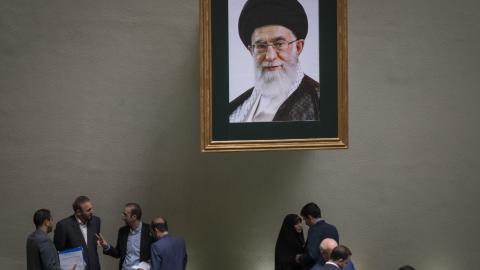 Iranian lawmakers talk to each other, while standing under a framed portrait of Iran's Supreme Leader, Ayatollah Ali Khamenei, during a public session of the Iranian Parliament in Tehran, Iran on April 22, 2025.(Morteza Nikoubazl via Getty Images)