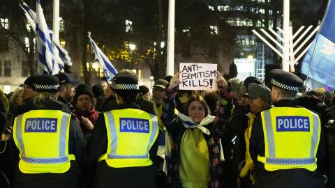 A woman holds up a sign that reads "anti-semitism kills" between police officers as people take part in a Hanukkah candle-lighting in central London on December 15, 2025. (Getty Images)